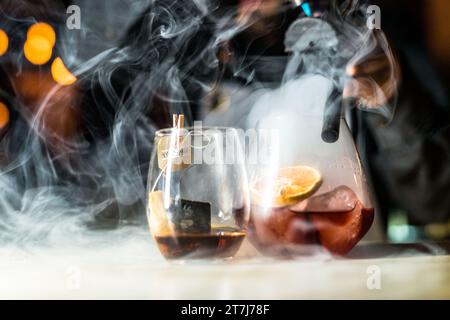Un barman préparant habilement deux cocktails dans des tasses chaudes de thé sur un comptoir Banque D'Images
