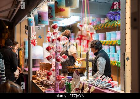 Sous la lueur festive, une femme fabrique des délices sucrés à la foire de Noël de la Sagrada Familia : pommes et bonbons au coton, créant une douce symphonie ag Banque D'Images