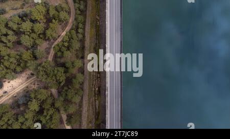 Vue aérienne d'une route sans véhicules qui divise un réservoir et une zone forestière au milieu de l'image. Concept de paysage Banque D'Images