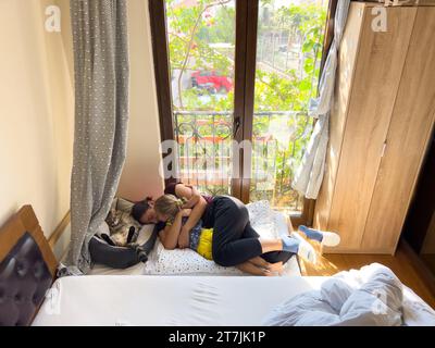 Maman et une petite fille sont couchées dans leurs bras sur un lit d'enfants dans une chambre à côté d'un chat Banque D'Images