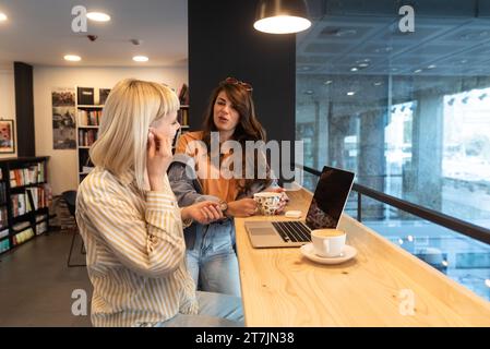 Jeune femme d'affaires freelance ou étudiant, expatrié ou vlogger se préparant pour le travail et l'appel vidéo en ligne Internet de librairie ou bibliothèque sur ordinateur portable com Banque D'Images