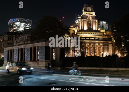 Le four Seasons Hotel au 10 Trinity Square, Londres est illuminé la nuit avec les gratte-ciel City of London en arrière-plan et la route en avant-plan Banque D'Images