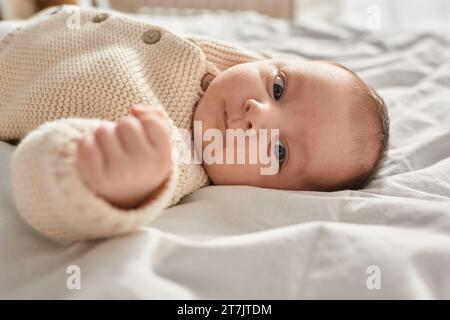 portrait d'adorable petit garçon nouveau-né dans un cardigan beige allongé sur le lit et regardant la caméra Banque D'Images