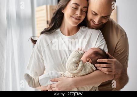 joyeux parents modernes dans des vêtements de maison confortables serrant chaudement et tenant leur fils nouveau-né amoureusement, famille Banque D'Images