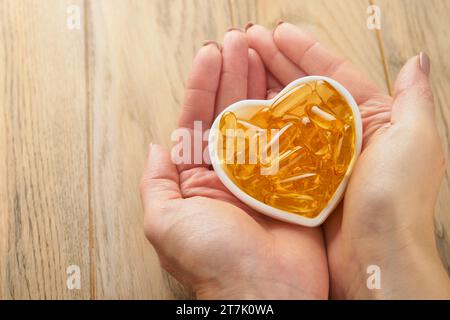 Femme ou médecin tient dans la main des capsules avec de la vitamine D, E ou des acides gras oméga 3,6,9 dans un bol en forme de coeur. Huile de poisson remplie d'huile de complément alimentaire. Naturel Banque D'Images