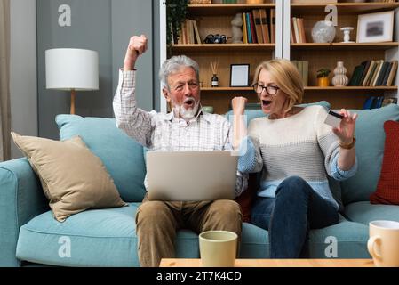 Joyeux vieux couple retraité moderne utilisant la carte de crédit et l'ordinateur portable pour les achats en ligne, acheter sur Internet, choisir la visite pour les vacances, faire le paiement wi Banque D'Images