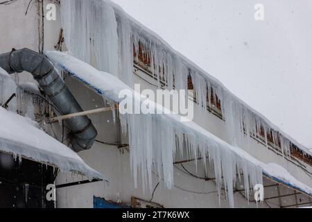 rangée de glaçons accrochée sur les bords du toit le jour d'hiver pendant la neige Banque D'Images