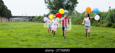 Les enfants avec des ballons courent dans le parc d'été Banque D'Images