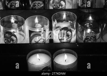 Sélestat, France - 25 décembre 2022 : les bougies de prière catholiques, avec la Sainte famille et Marie avec l'enfant Jésus, brillent dans l'église la veille de Noël. Noir blanc Banque D'Images