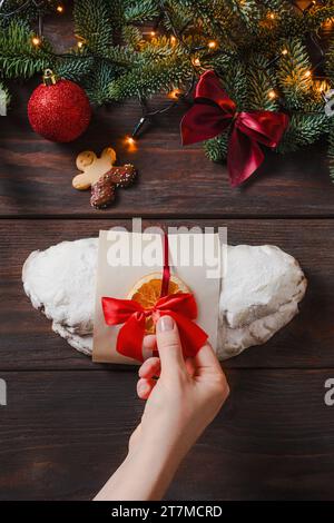 Stollen de Noël avec massepain et fruits secs sur fond sombre. Lumière de Noël festive, ambiance de vacances, temps joyeux. Les mains féminines décorent stoll Banque D'Images