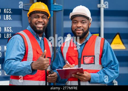 Portrait de deux ingénieurs ou contremaîtres africains portent un EPI vérifiant le stockage du conteneur avec le fond du conteneur de fret au coucher du soleil. Logistique importation globale ou Banque D'Images