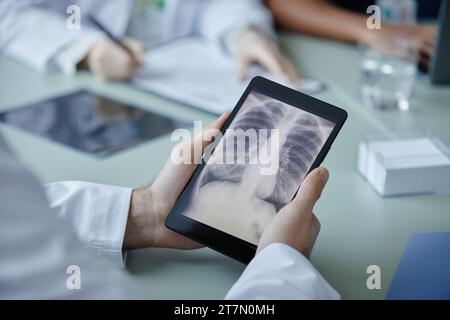 Gros plan d'un médecin méconnaissable tenant une tablette numérique avec une image de radiographie thoracique à l'écran pendant la réunion dans la clinique, espace de copie Banque D'Images