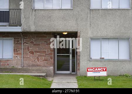 Signe de vacance sur la pelouse devant l'entrée de l'immeuble d'appartements plus ancien. Banque D'Images