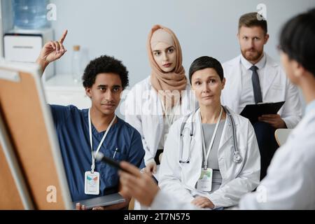 Portrait d'un jeune homme du Moyen-Orient levant la main dans l'audience d'un séminaire médical Banque D'Images