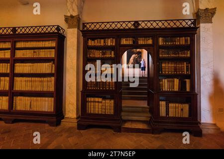 Asciano, Italie : un touriste monte un escalier au milieu des étagères de la bibliothèque le monastère dramatique d'Oliveto, Monte Oliveto Banque D'Images