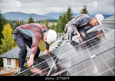 Techniciens professionnels ajustant les cellules photovoltaïques solaires. Installation d'un panneau solaire. Deux travailleurs masculins fixant soigneusement la batterie sur un toit. Banque D'Images