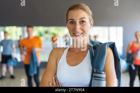 Femme souriante avec sac de gym et bouteille d'eau dans un centre de fitness avec des gens en arrière-plan. Image conceptuelle du travail d'équipe Banque D'Images