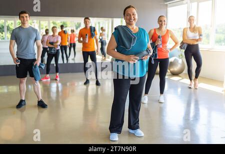 Groupe diversifié de sportifs avec équipement de fitness dans une salle de gym lumineuse, souriante et prête à s'entraîner. Image conceptuelle du travail d'équipe Banque D'Images
