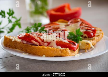 sandwich chaud de pain grillé frit avec des poivrons cuits au four et du fromage, dans une assiette sur une table en bois Banque D'Images