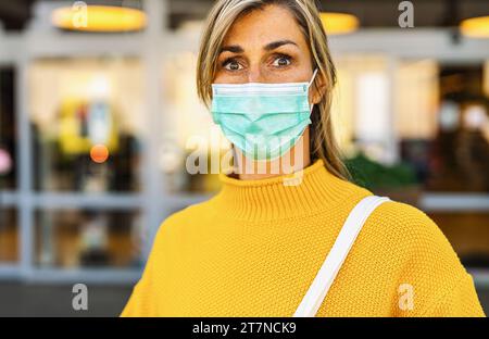 Gros plan d'une femme dans un pull jaune portant un masque facial à la pandémie de corona, regardant la caméra Banque D'Images