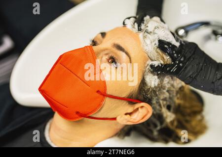 Gros plan d'une femme dans un masque rouge se faisant laver les cheveux dans un salon Banque D'Images