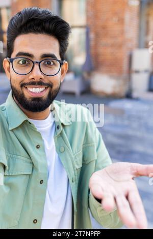 Vue de la caméra Web du téléphone, jeune homme utilise l'application sur le smartphone pour la communication d'appel vidéo à distance, l'homme indien sourit et regarde la caméra, agite la main dans le salut. Tir vertical Banque D'Images