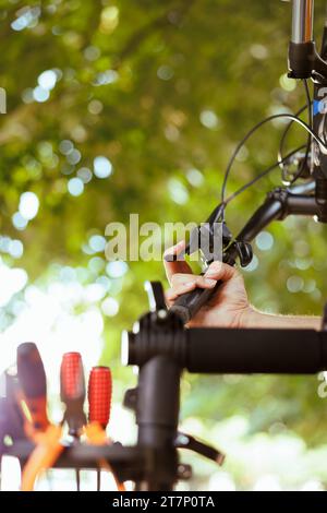 Image détaillée du bras de l'homme caucasien maintenant la partie de vélo comme entretien annuel d'été. L'image montre une personne qui vérifie et règle les leviers de frein et les leviers de changement de vitesse de vélo dans la cour d'origine. Banque D'Images