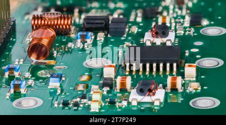 Vue rapprochée de composants électroniques montés en surface dans des circuits radiofréquence de syntoniseur de télévision. Micropuce semi-conducteur et bobines à noyau d'air sur un circuit imprimé vert. Banque D'Images