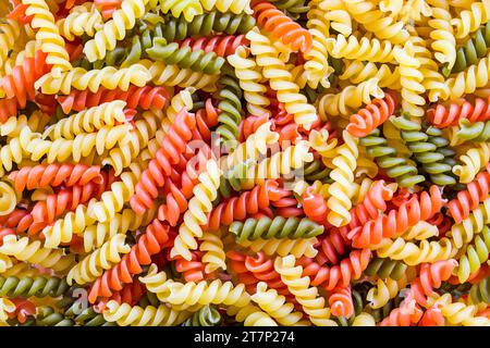 Gros plan de pâtes de variété fusilli de trois couleurs dans une belle texture colorée. Beaucoup de rotini secs crus jaune, rouge ou vert de couleur, saveur tomate ou épinard. Banque D'Images