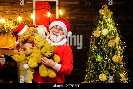 Sourire Père Noël avec des jouets ours en peluche dans la chambre décorée pour Noël. Homme barbu en costume de Père Noël avec des ours en peluche. Noël ou Nouveau Banque D'Images