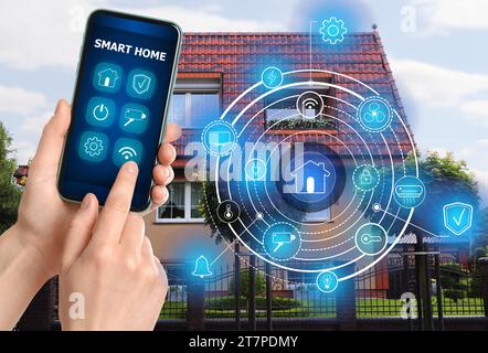 Femme utilisant le système intelligent de contrôle de la maison via l'application sur le téléphone mobile à l'extérieur, closeup. Schéma sur la maison Banque D'Images