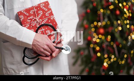 Concept de bannière médicale pour Noël et nouvel an.médecin féminin en manteau blanc tient stéthoscope et boîte-cadeau enveloppé dans du papier rouge sur fond o Banque D'Images