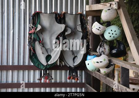 Équipement d'escalade - casques colorés et gilets de sécurité accrochés à une planche dans un parc de corde en gros plan Banque D'Images