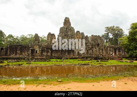 Une photo du temple de Bayon prise de l'entrée nord. Les sculptures de visages sereins sont visibles sur les tours de grès et une statue assise peut l'être Banque D'Images