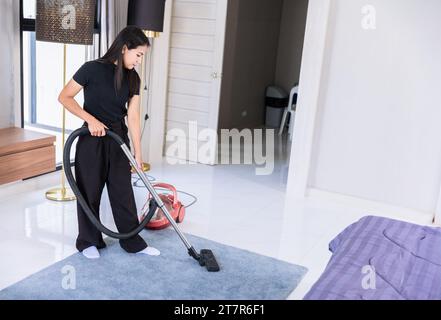 Femme femme de ménage faisant la corvée, femme de maison aspirateur nettoie la moquette de plancher de poussière dans la chambre. Banque D'Images