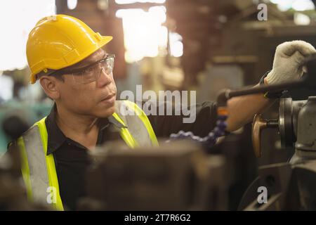 Travailleur technicien ingénieur asiatique portant un casque de protection des yeux de casque de sécurité Focus processus de production manuel de machine de contrôle de compétence dans l'usine de métal Banque D'Images