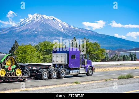 Tracteur de semi-camion carrier big RIG violet avec cabine allongée pour le repos du conducteur de camion transportant de l'équipement sur le pont marchepied semi-remorque fonctionnant sur le roa Banque D'Images