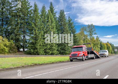 Camion semi-remorque rouge compact à cabine de jour moyenne avec plate-forme de remorque élévatrice, prenez la mini-fourgonnette commerciale cassée sur l'épaule de la route Banque D'Images