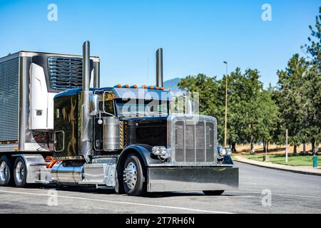 Tracteur semi-camion industriel long porteur noir classique big rig avec semi-remorque de réfrigérateur chargé se tenant sur la zone de repos de la route d'autoroute p Banque D'Images