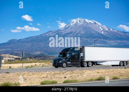 Long transporteur industriel porte-bagages noir big rig semi-camion transportant des marchandises dans le réfrigérateur semi-remorque fonctionnant sur la large autoroute multiligne d'été r Banque D'Images