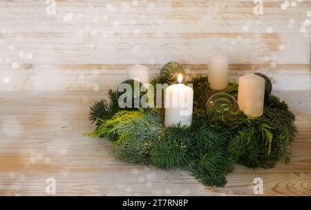 Premier avènement, couronne de l'AVENT naturel avec des bougies blanches, on est allumé, boules de Noël vertes en verre, fond en bois avec bokeh enneigé, copie Banque D'Images