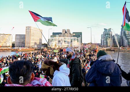 Un homme en bandana agite le drapeau palestinien comme manifestants lors d'une marche pour la Palestine à travers le pont Vauxhall dans le centre de Londres sous l'œil vigilant du bâtiment MI6 Banque D'Images