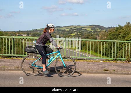 Cycliste féminine chevauchant Whyte sport vélo traversant au-dessus de l'autoroute M61 sur un pont in près de Manchester UK Banque D'Images