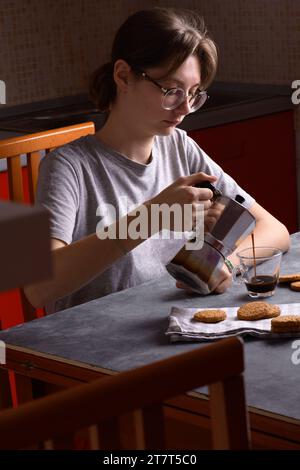 Jeune femme versant le café du pot de moka dans la tasse dans la cuisine Banque D'Images