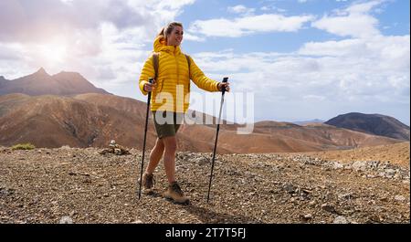 Randonneur en veste jaune avec bâtons de trekking sur un sentier de montagne sous un ciel nuageux Banque D'Images