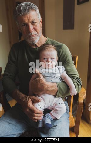 Grand-père tenant bébé petite-fille, les deux visages sérieux Banque D'Images