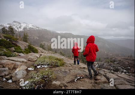 Deux adolescents en randonnée rouge le long d'un rocher de granit avec montagne enneigée Banque D'Images