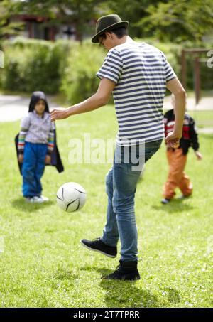 Maternelle, enseignant et jouer au football avec les enfants sur l'herbe, la pelouse ou le terrain avec le jeu ou le sport. Football, ballon ou enfants avec l'entraînement de l'homme à coup de pied ou Banque D'Images