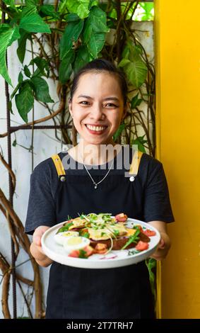 Jeune serveuse vietnamienne tenant une assiette avec du pain grillé au poulet Banque D'Images