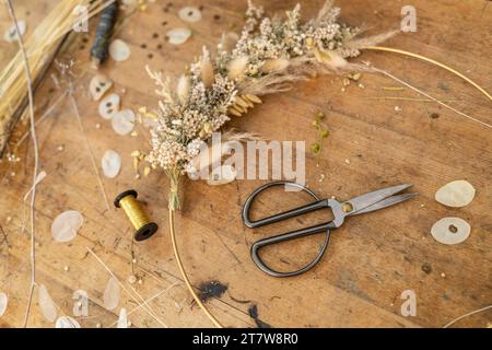 Arrangement de fleurs séchées et ciseaux sur une table en bois avec pétales éparpillés et bobine de fil Banque D'Images